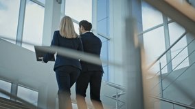 Two colleagues walking upstairs corporate office building. Elegant businesswoman showing papers folder to businessman talking smartphone. Business partners discussing project strategy going up stairs. - Powered by Shutterstock - Get 15% off with code: PIKWIZARD15
