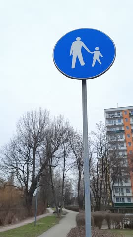 pedestrian zone sign in residential area, pedestrian crossing symbol in neighborhood district with apartment building and trees in background. Urban infrastructure, pedestrian zones, road safety