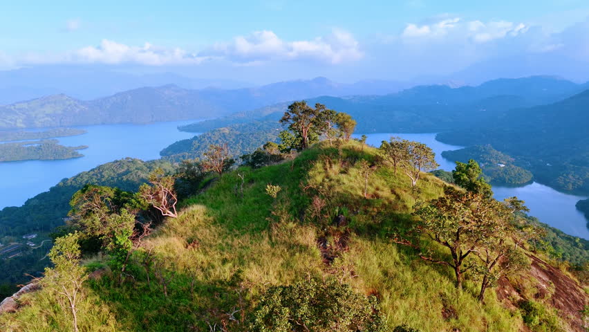 Top of the mountain covered with grass and some trees. Beautiful lakes and rocky silhouettes in the fog at backdrop.
