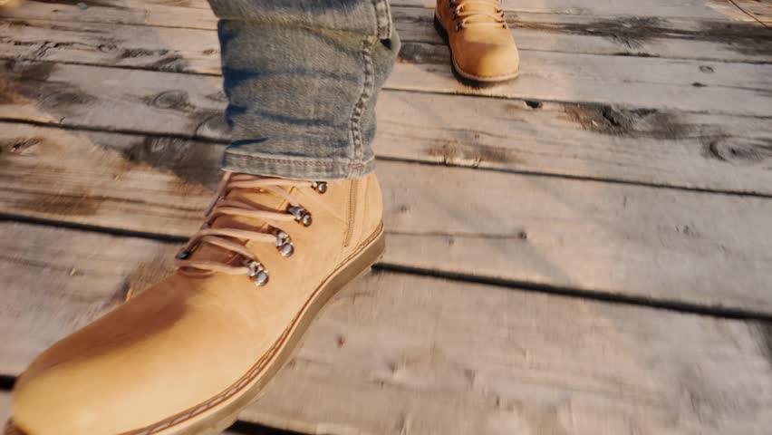 Man In Hiking Boots Walking Across A Wooden Suspension Bridge Over A Beautiful Mountain Lake. Experience The Excitement Of An Epic Outdoor Adventure Through Stunning Scenery.