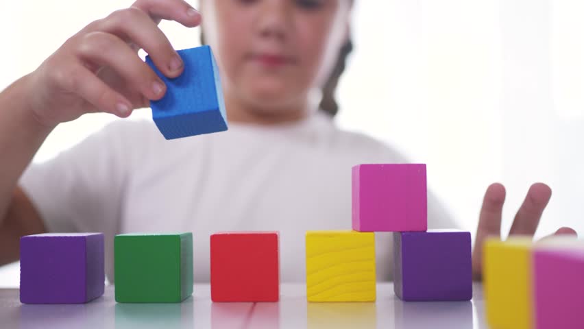 A girl plays with blocks and toys in kindergarten. Constructor little child concept. The girl daughter is playing with cubes. Girl collects toys from lifestyle a stack of cubes.