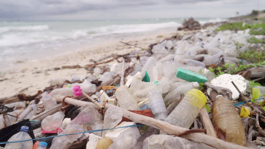 Mixed plastic waste pollution on beach, ocean in background, marine debris, water bottles