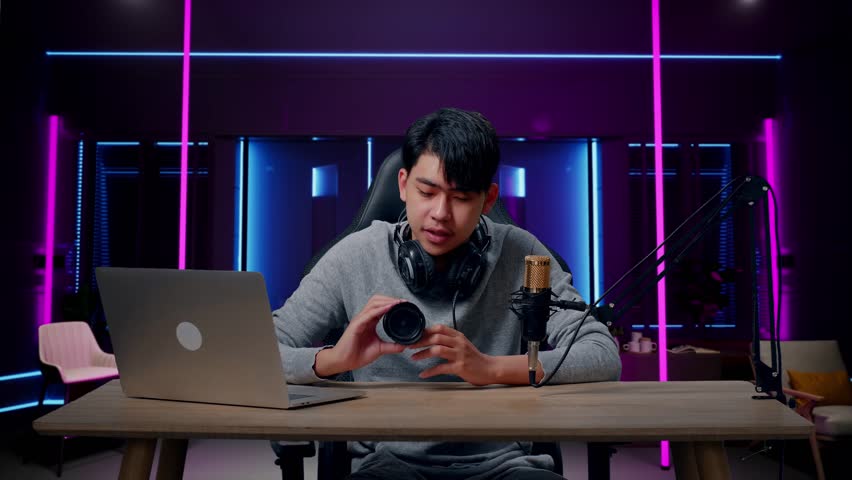 A Smiling Asian Man With Computer Reviewing Camera Len In Room Lit By Neon Lights In Retro