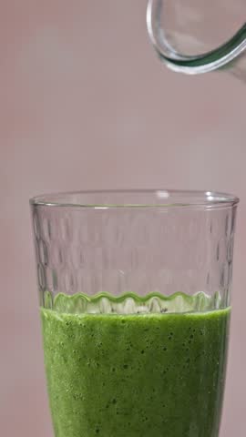 freshly made green and pink strawberry and spinach smoothie flows into a glass from a bottle on a light background
