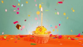 Delicious orange cupcake with a single lit candle on top, placed on an orange surface in front of a green wall, decorated with green, yellow, and red confetti sprinkles. - Powered by Shutterstock - Get 15% off with code: PIKWIZARD15
