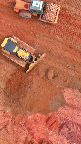 Construction workers utilize heavy machinery to grade, prepare red soil tamping, leveling for building projects at building site