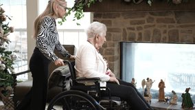A daughter assists her elderly mother in a wheelchair while enjoying time together beside a beautifully decorated fireplace with festive figures. - Powered by Shutterstock - Get 15% off with code: PIKWIZARD15