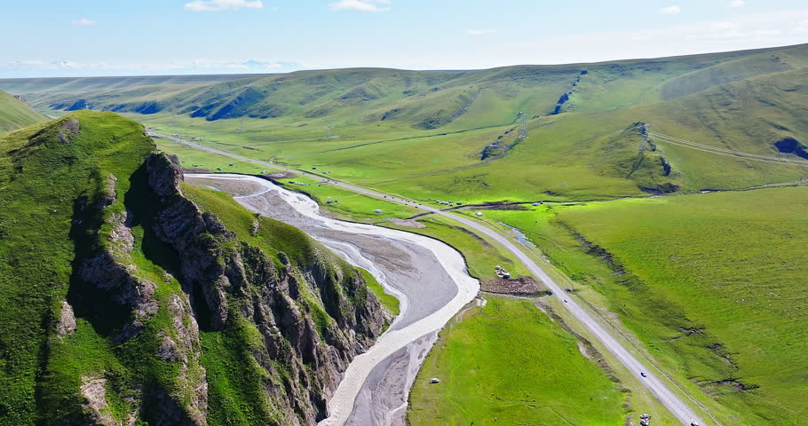 Aerial view of curving river and highway road with green grassland on a sunny day. Beautiful scenery along the Duku Highway in Xinjiang, China.