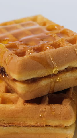 Vertical video. Hand pouring golden honey on waffles with crisp apple slices