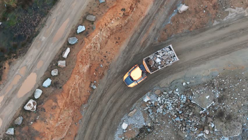 An excavator loads rock onto a massive truck, transporting it to the crusher. A quarry scene with heavy machinery running at full capacity.