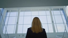 Back view businesswoman walking up stairs inside corporate office. Elegant woman executive going upstairs in modern building lobby. Unknown blonde entrepreneur in stylish suit at business environment. - Powered by Shutterstock - Get 15% off with code: PIKWIZARD15