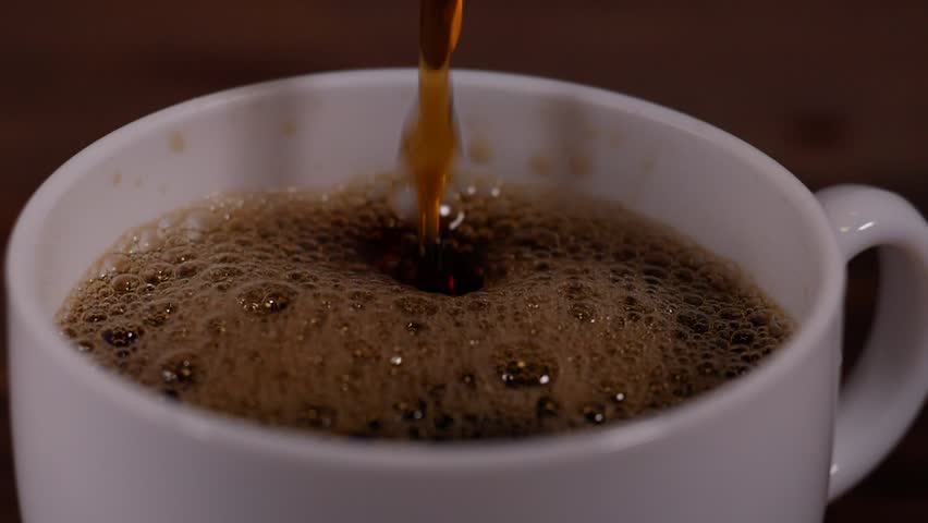 coffee being poured into a white ceramic cup, showcasing the dark liquid with a rich and aromatic foam layer.