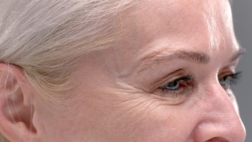 Close up portrait: blue eye of an old blonde woman with large wrinkles. Smile of a senior female, elderly retired beauty care. Product for skincare with natural anti-aging cosmetics, mascara eyelashes