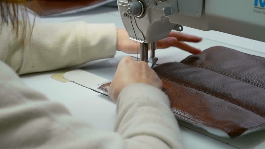 Working sewing machine stitching leather. Tailor's hands holding sewing leather carefully. Manufacturing handicraft accessories for furniture.
