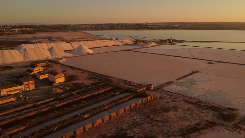 Camera panning over the salt evaporation ponds of torrevieja pink lake at sunset, with large piles of salt