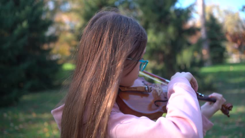 Adorable Caucasian girl playing violin in a sunny park, embracing the joy of music education. Cute Caucasian little girl playing the violin in the park, education music concept. 