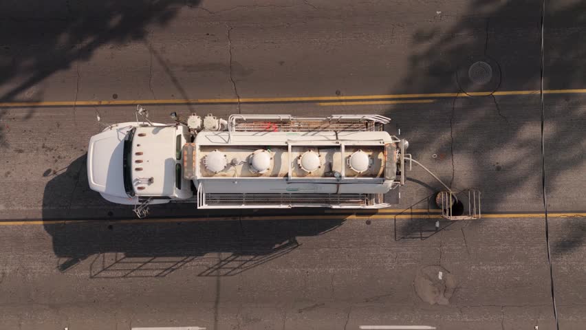 An Aerial View Capturing a Tanker Truck Positioned Above a Drain on a Busy Road during Peak Traffic Hours