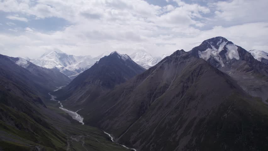 View of the gorge with snow peaks in the distance. The drone is flying smoothly. A river runs through the gorge. High mountains with the majestic peak of Khan Tengri. A marble wall made of ice. Cloudy