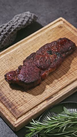 Chef slicing freshly grilled juicy beef wagyu steak meat with a knife on a wooden cutting board in the kitchen, food close-up, zoom in
