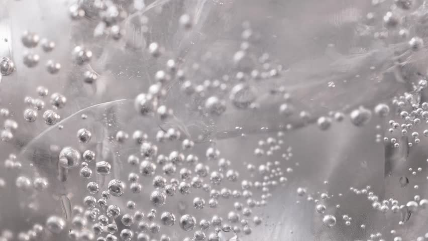 Close-up of a sparkling carbonated drink with bubbles, zoom in macro, neutral color. Soda with ice and bubbles. Sparkling cold soft drink, carbonated liquid and cool iced tonic in a glasses. Soda fizz
