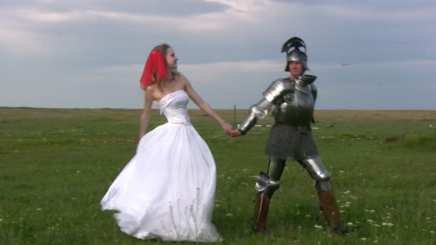Man in medieval armor is excellent for hand girl in a white wedding dress on the