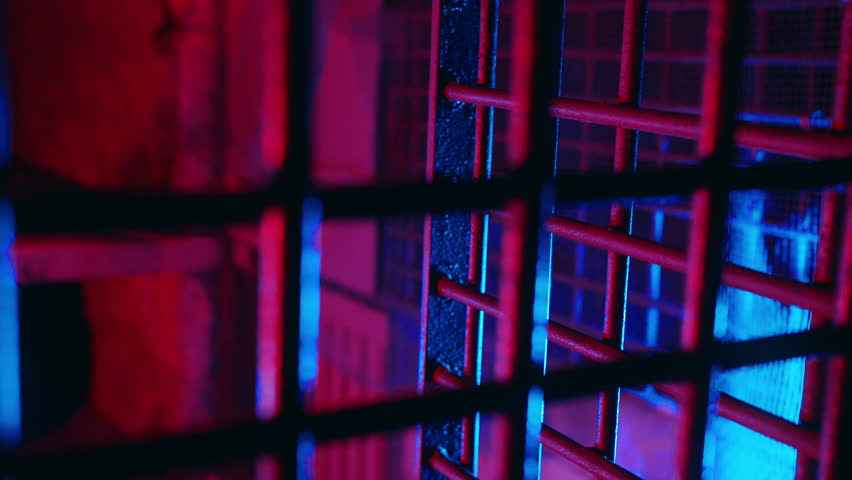 Cinematic metal bars in scary dungeon cell for torture. Abandoned prison. Creepy cage underground. Thriller jail lit with ambient red and blue neon light. Ancient underground chamber. Old prison grate