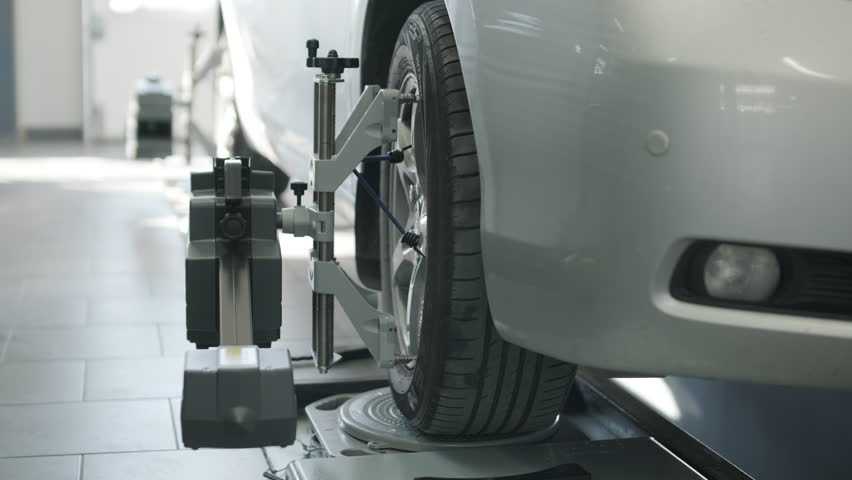 Mechanic performing a wheel alignment process in a modern workshop. Professional equipment is used to ensure accurate vehicle alignment for optimal performance and safety
