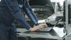 Mechanic in uniform sitting in a car performing diagnostics with a laptop. Modern automotive workshop setting with a focus on technology and vehicle maintenance - Powered by Shutterstock - Get 15% off with code: PIKWIZARD15