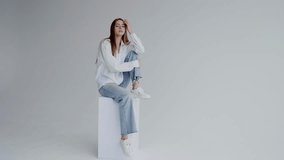 Portrait of a young woman dressed in a relaxed white shirt and jeans, seated confidently against a plain background, expressing a serene and approachable attitude. Young Woman in Casual Outfit Posing - Powered by Shutterstock - Get 15% off with code: PIKWIZARD15