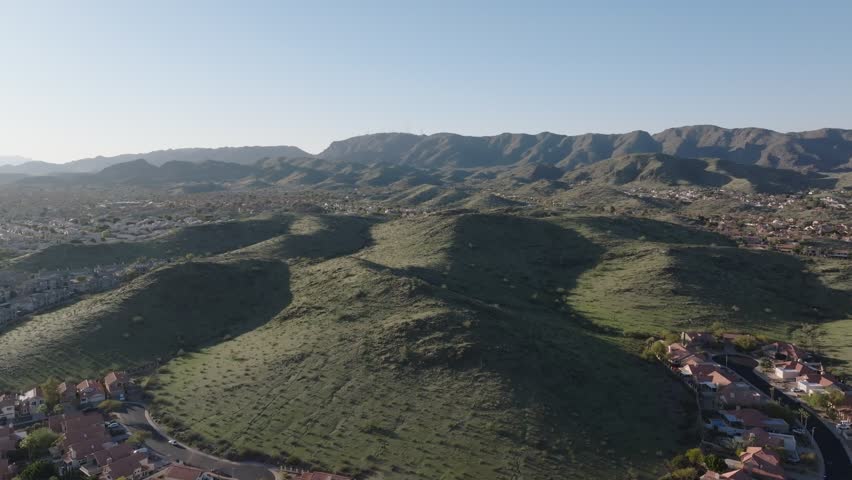 Rolling green hills surrounded by neighborhoods and distant mountains under a clear blue sky