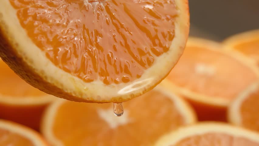 A drop of orange juice drips from the cut of an orange half. Slow motion. High quality 4k footage