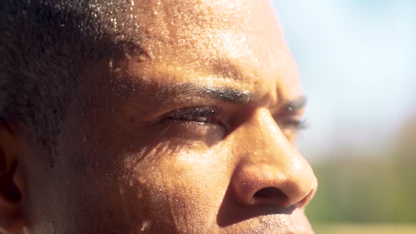 Close-up of focused African American athlete sweating after an intense outdoor workout. Determined male catching his breath under a clear, blue, sky while recovering from physical exertion - Powered by Shutterstock - Get 15% off with code: PIKWIZARD15