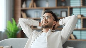 Smiling handsome bearded man relaxing with his eyes closed and his hands behind his head while sitting on sofa in living room at home. Positive happy male freelancer in shirt resting after work - Powered by Shutterstock - Get 15% off with code: PIKWIZARD15