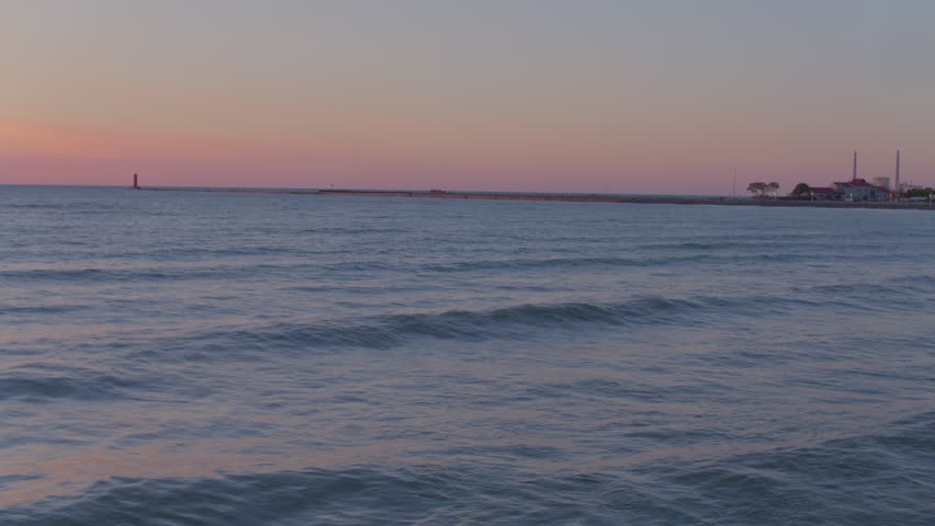 Low-angle view of gentle waves on Lake Michigan at sunrise in Sheboygan, Wisconsin with lighthouse on the horizon. Serene morning light, calm water, and ombre sky. Ideal for nature and travel themes