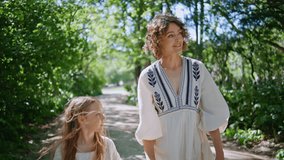 Mother daughter strolling park at sunny day closeup. Relaxed woman holding girl hand walking on sunlight path. Carefree mom child wearing dresses enjoy weekend together. Family relationships concept  - Powered by Shutterstock - Get 15% off with code: PIKWIZARD15