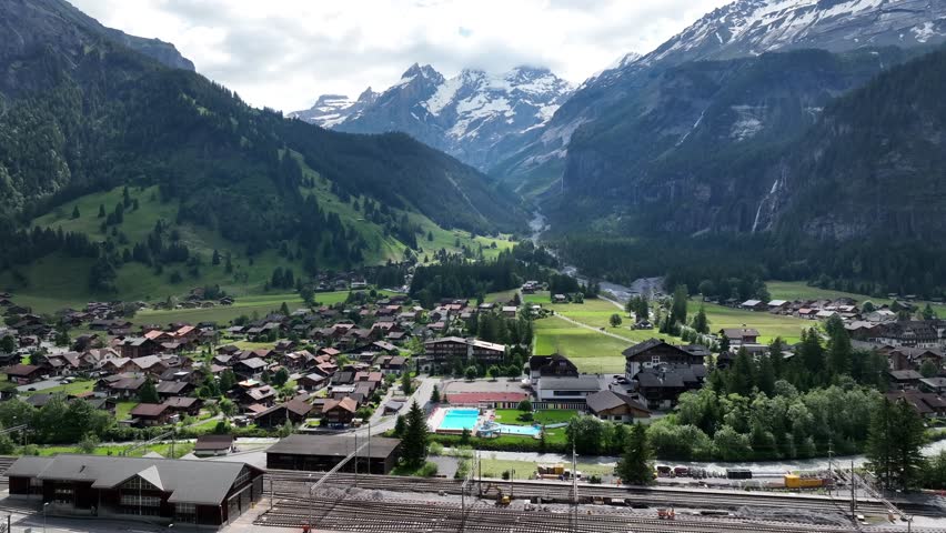 Aerial view overlooking quaint Swiss holiday village neighbourhood under grand snowy mountain range