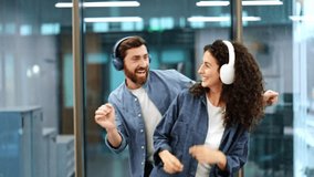 Smiling business colleagues enjoy listening to music through headphones in a modern office. Happy man and woman are dancing and having fun during a break at work. - Powered by Shutterstock - Get 15% off with code: PIKWIZARD15