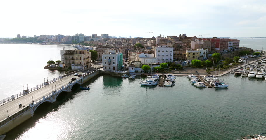 Cars Driving Through The Road Bridge Over The Sea With Historic Center Of Taranto In Apulia, Italy. - aerial shot