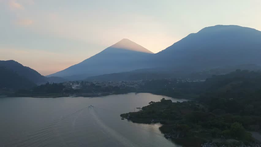 Landscape of small towns and large mountains surrounding Lake Atitlan, with a view of the sunset in dense fog, Guatemala