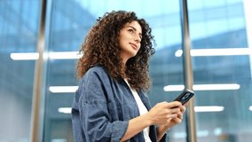 Confident young businesswoman using smartphone in modern office building. Curly haired woman in casual clothes browsing internet on cellphone. - Powered by Shutterstock - Get 15% off with code: PIKWIZARD15