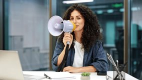 Young business woman with curly hair speaking into a megaphone. She is sitting at her desk in a modern office. - Powered by Shutterstock - Get 15% off with code: PIKWIZARD15