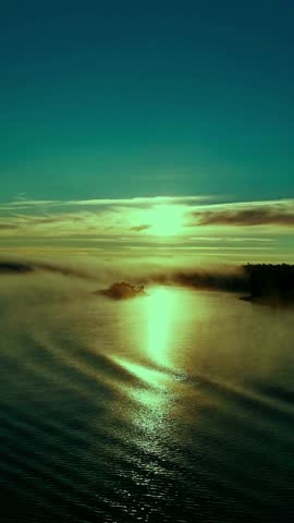 A photo of a serene lake at sunrise or sunset, with fog or mist hanging over the water and a small island reflecting the sunlight.