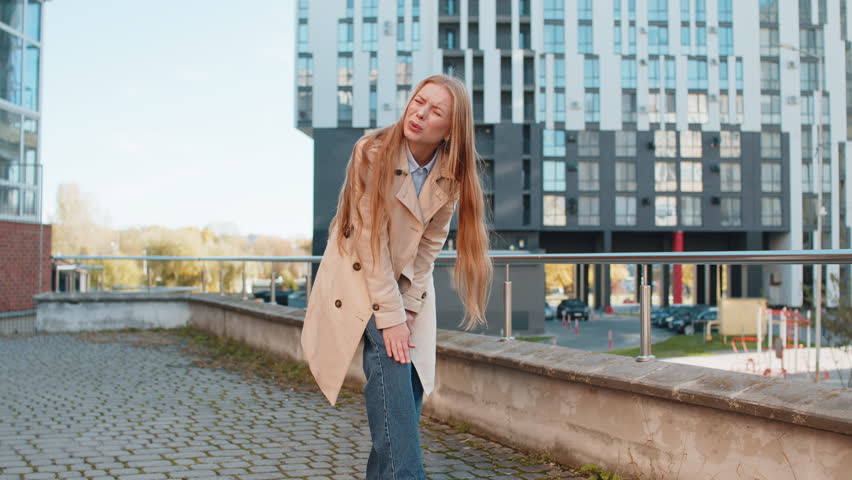 Sick sad mature businesswoman suffer from painful discomfort severe knee joint ache, leg muscles, could not walk outdoors. Girl woman massaging knees illness cramps rheumatism on urban city street.