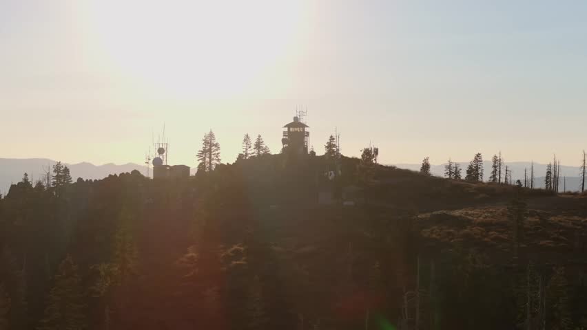 Mountain fire lookout tower sits atop a forested ridge at sunrise with distant hazy mountains