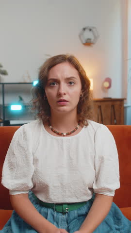 Young woman feeling hopelessness and loneliness, nervous breakdown, loses play game becoming surprised by lottery results, bad fortune, loss, unlucky news. Upset girl on sofa couch at home. Vertical