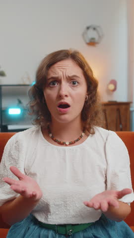 Young woman feeling hopelessness and loneliness, nervous breakdown, loses play game becoming surprised by lottery results, bad fortune, loss, unlucky news. Upset girl on sofa couch at home. Vertical