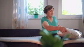 Senior woman arranging cushions on a sofa in a cozy, sunlit living room. Concept of homemaking, routine, and comfort in a relaxed domestic environment - Powered by Shutterstock - Get 15% off with code: PIKWIZARD15