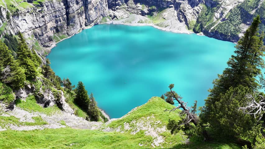 Slow drone flight above grassy cliffs high above the Oeschinensee lake in the  Swiss Alps. Down view towards the turquoise blue lake. Beautiful Swiss mountains, amazing nature. Outdoor adventure, heal