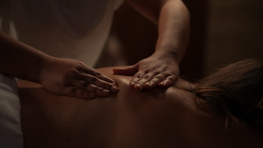 Skilled massage therapist working on client female back, delivering soothing treatment in spa salon with softly illuminated wellness environment, close-up. Concept of rest with spa treatment.