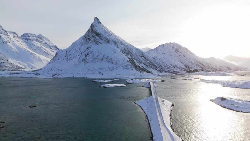 Flying over a snow covered road bridge at Lofoten, northern Norway towards the famous mountain at sunrise in winter
